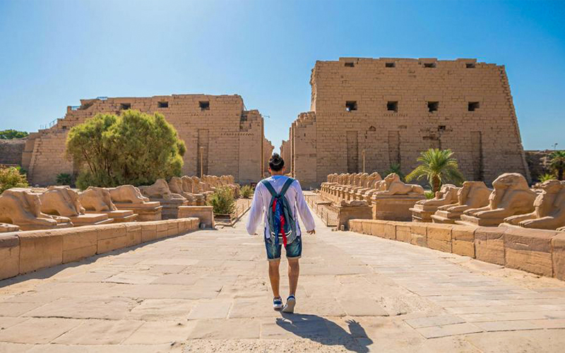a tourist is enjoying the beautiful corridor ram sculptures and the grand sanctuary of amun in the karnak temple